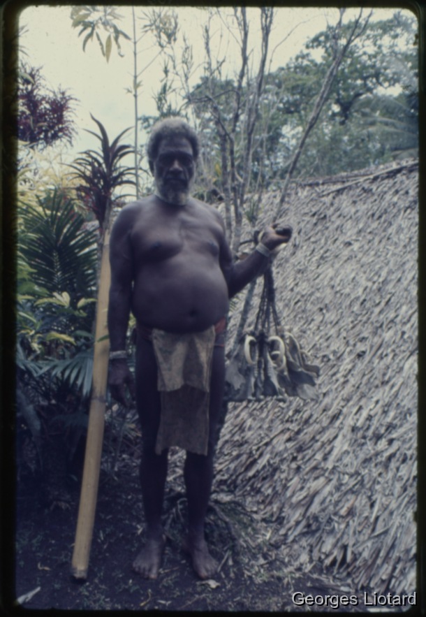 Ilôt  MALO / Le vieil homme présente un ensemble de machoires reliées entre elles par des cordelettes en fibres de coco. Ces cordelettes sont nouées vers le haut de façon à former une ganse par laquelle le pendant sera suspendu au toît de l'abri / Georges Liotard / Villages d'Abunaress et de Narombe - Ile Malo - Vanuatu