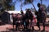 Kids dance in the park with one woman conducting them and two women watching them